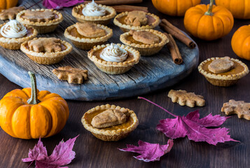 a platter of pumpkin pie tarts surrounded by pumpkins and fall leaves