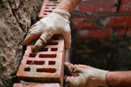 Hands senior man mason of putting a brick on cement