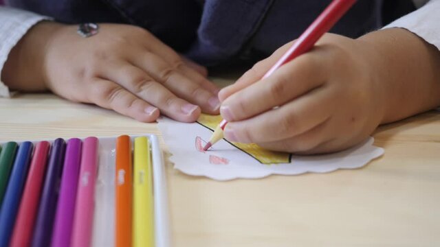 The child draws with his left hand and a colored pencil.
