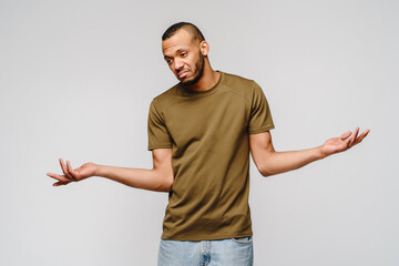 I don't know gesture - Young afrcian american man over grey background being at a loss, showing helpless gesture with arm and hands, as if he does not know what to do