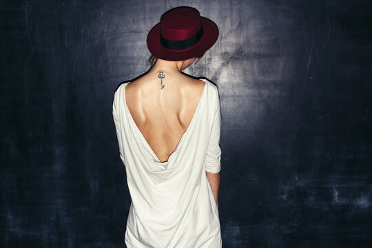 Sexy open back dress. Young woman posing alone showing her key tattoo and red hat