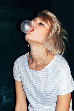 Fashionable sexy blonde woman with red lips is blowing bubble-gum ball