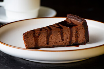 Slice of chocolate cake on a white plate on a dark background