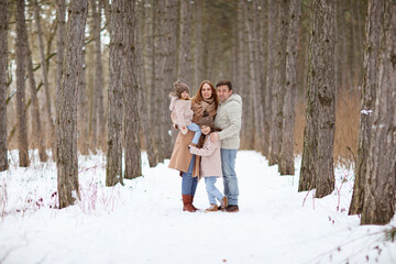 father and mother with their little daughters in the snowy winter forest. travel and recreation with children in winter. family walks in the fresh air during the new year holidays.