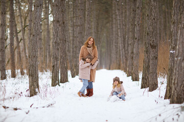 mother with little daughters in a snowy winter forest. travel and recreation with children in winter. family walks in the fresh air during the new year holidays.