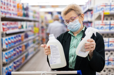 mature woman chooses disinfectants and detergent in household chemicals department in supermarket