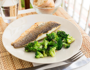 fried fillet of sea bass with garnish of broccoli on black warm stone plate