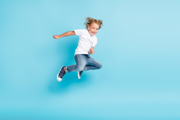 Fototapeta na wymiar Little kid jump motion funny grimace hands wear white shirt jeans sneakers isolated blue color background
