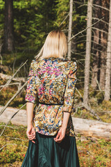 Blonde woman with colorful blouse and green dress walking in the dense and dark forest