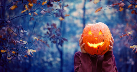 Boy holding carved pumpkin for halloween in front of his head in dark autumn forest. Halloween...