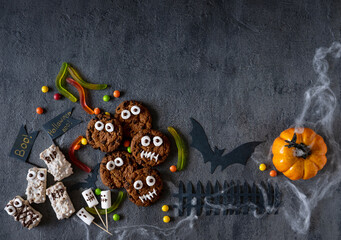 Modern Halloween background. Halloween candy bar: funny monsters made of biscuits with chocolate and ghosts marshmallow close-up on the table. Halloween party decoration. Trick or treat concept.