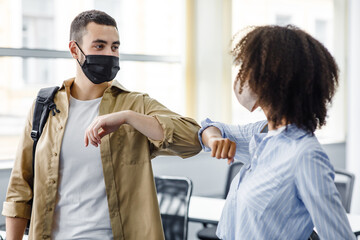 Fototapeta premium Modern hello at protection against coronavirus epidemic at work. Arabian young man and african american woman greet each other in morning in interior of modern office