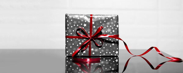 Grey gift box with red bow on black glass, background of white. Holidays or Black Friday concept.