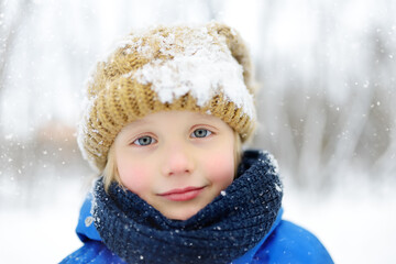 Funny little boy in blue winter clothes walks during a snowfall. Outdoors winter activities for kids.