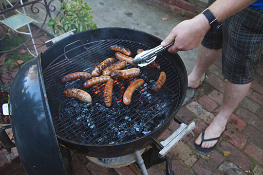 Man grilling sausages on kettle bbq with coal / charcoal