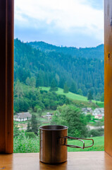 Fototapeta na wymiar Metal cup of tea stands on a wooden window sill against the backdrop of the mountains