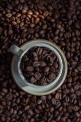 Coffee beans in light brown cup on the coffee beans background top view