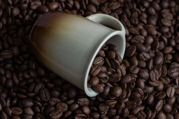 Coffee beans in light brown cup on the coffee beans background top view