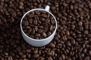 Coffee beans in white cup on the coffee beans background top view