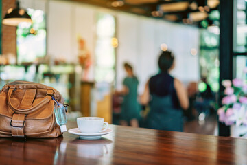 Mini alcohol gel bottle to kill Corona Virus(Covid-19) hang on a brown leather shoulder bag with hot coffee on table in cafe.New normal lifestyle.Health care concept.Selective focus on alcohol gel