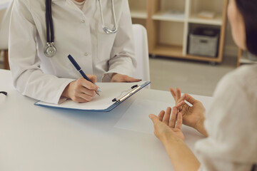 Hands of a female doctor writing notes to a patient about a medical examination or prescription.