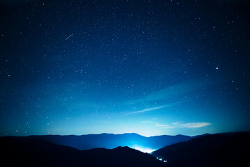 Starry sky over mountains panorama with city lights below