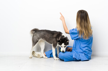 Veterinary doctor with Siberian Husky dog sitting on the floor pointing back with the index finger