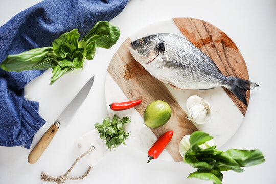 Fresh sea bream and ingredients for cooking it on white background.