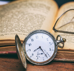 Pocket watch and old books on a wooden office desk background.