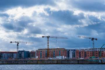 Fototapeta premium A construction site with three cranes, construction site in Berlin, Germany, three cranes on a construction site, dark clouds, Housing construction in Berlin