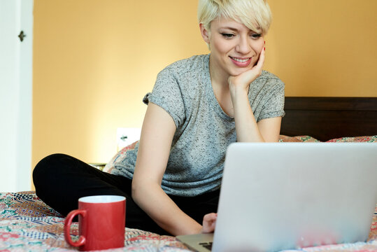 smiling woman sitting on bed with laptop