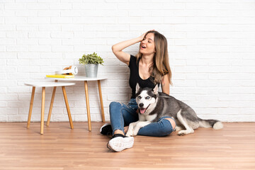 Young pretty woman with her husky dog sitting in the floor at indoors has realized something and...