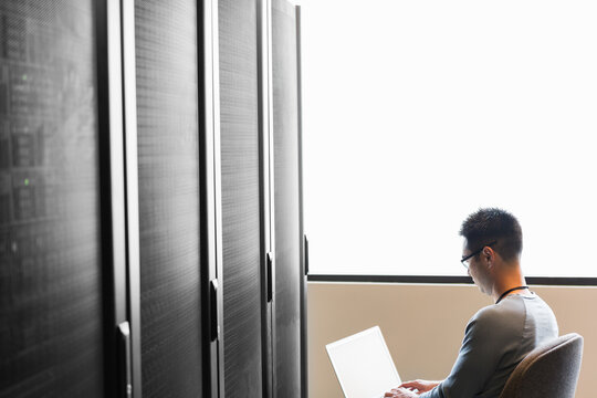Technician sits backlit in front of server working on laptop