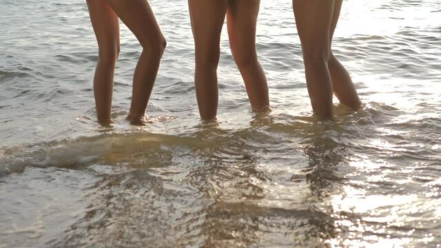 Leg of three beautiful girls having fun, dancing and splashing water in the sea at the beach on beautiful summer sunset.