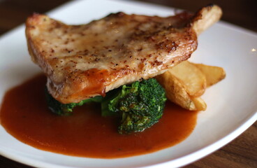 Close up of a plate of delicious grilled pork chop served with broccoli and french fries