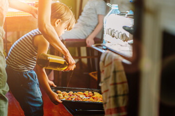 Cute little preschooler boy in striped t-shirt help his mother at kitchen. Cook at home. Young woman pouring oil at a baking tray before oven. Her son helping hold. Family cooking dinner together