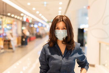 Beautiful middle aged Asian woman cover mouth and cough, wear medical face mask to protect from infection of viruses, pandemic, outbreak and epidemic of disease in city shopping mall.