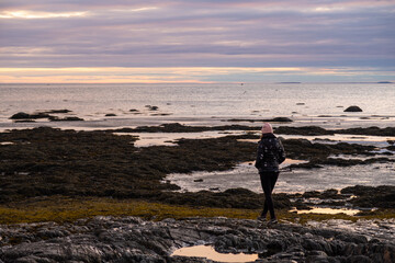 Back view of a woman walking on the shore in the Bic national park, at sunrise, Canada