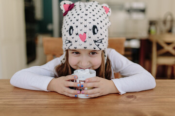 Cute young girl in a winter hat drinking hot chocolate with marshmallows