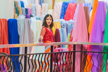 Woman wearing Traditional India costume carrying shopping bags while walking in the fabric shop and Many color fabric rolls on background.