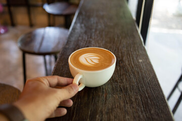 Hand put a Latte arts coffe hot coffee on wooden table.barista love art concept.