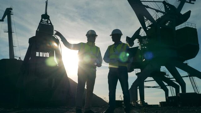 Male engineers are having a discussion near port cranes