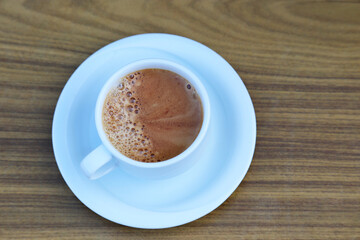 Cup of cappuccino coffee in a white saucer on wooden table, top view