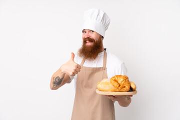Redhead man in chef uniform. Male baker holding a table with several breads with thumbs up because something good has happened