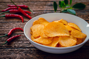 Spicy potato chips in white bowl and chili on wooden table