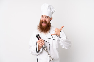 Redhead man using hand blender over isolated white background making phone gesture