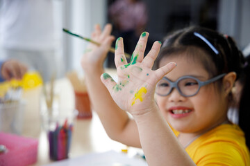 Asian girl with Down's syndrome painting her hand.