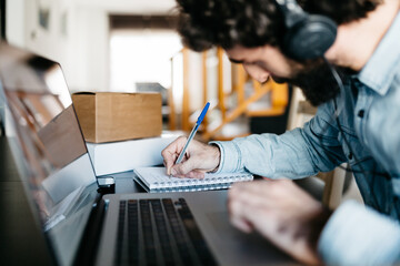 Busy man writing down in planner at laptop.