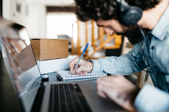 Busy man writing down in planner at laptop.