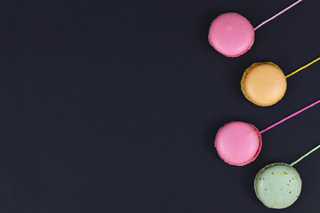 Colorful French macaron attached to strings at side of black background with empty copy space
